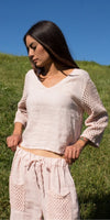 Woman wearing light pink linen top with crochet sleeves and matching drawstring pants outdoors
