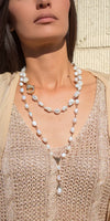 Woman wearing layered freshwater pearl necklaces over a beige knit top in sunlight