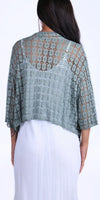 Woman wearing sage green open-knit crochet poncho over a white dress, back view