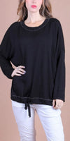 Woman wearing a loose black long sleeve top with drawstring hem and white pants