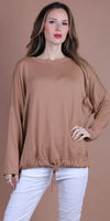 Woman wearing a loose tan knit top with drawstring hem and white pants, neutral background