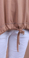 Close-up of tan knit drawstring top hem paired with white pants, women's fashion