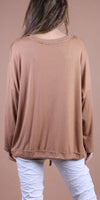 Back view of woman wearing loose brown long sleeve top and white ruched pants