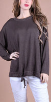 Woman wearing a loose brown knit sweater with drawstring hem and white pants