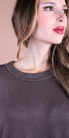 Woman wearing a brown crew neck knit top, close-up on neckline and face, neutral background