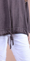 Brown knit top with drawstring hem and white linen pants, close-up on waist detail