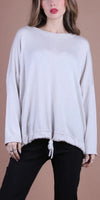 Woman wearing loose beige knit sweater with drawstring hem and black pants