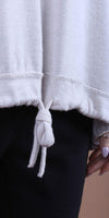 Close-up of a cream drawstring sweater hem with knot detail, paired with black pants