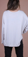 Back view of woman wearing a loose light beige long sleeve top with black pants
