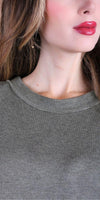 Close-up of woman wearing olive green knit sweater, natural makeup, and drop earring