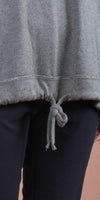 Close-up of a grey knit women's sweater with drawstring hem and black pants