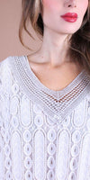 Woman wearing a white lace V-neck blouse with intricate patterns and openwork details
