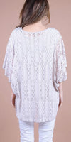 Woman wearing a white lace blouse with batwing sleeves and light pants, back view