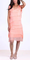 Woman wearing a sleeveless peach fringe dress with a sheer hem, standing against white background