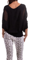 Woman wearing a sheer black blouse and white snake print pants, shown from the back