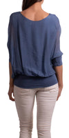 Woman in a loose blue blouse with batwing sleeves and beige pants, shown from behind