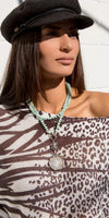 Woman wearing a black newsboy hat, mint beaded necklace, and animal print top