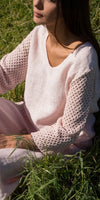 Woman in light pink linen top with crochet sleeves sitting on grass in sunlight