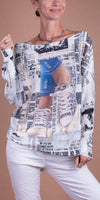 Woman wearing a newspaper print long-sleeve top with sneakers graphic, paired with white pants.
