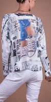 Woman wearing a printed newspaper-style sweater with sneaker graphic, paired with white pants