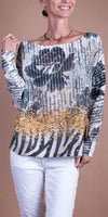Woman wearing a patterned knit sweater with gold accents and white pants, standing indoors