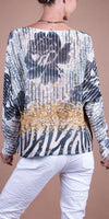Back view of a woman wearing a patterned knit sweater with gold accents and white pants
