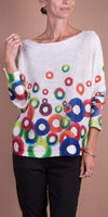 Woman wearing a white knit sweater with colorful circular patterns and black pants