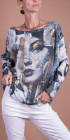 Woman in graphic print sweater with abstract female face design and white pants