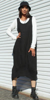 Woman in black linen dress over white long sleeve shirt, black boots, and a black hat standing outdoors