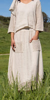 Woman wearing a beige linen dress with crochet details and pockets, outdoors in a grassy field