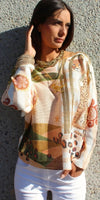 Woman wearing a patterned long-sleeve top with animal print accents and white pants in sunlight