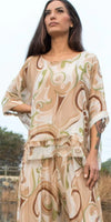 Woman wearing flowy beige and green patterned silk top and pants set outdoors