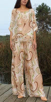 Woman wearing beige and green abstract print silk top and wide leg pants by a lakeside