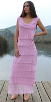Woman in sleeveless pink tiered maxi dress with frayed edges, standing on a wooden dock by a lake