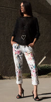 Woman wearing black knit sweater and floral print white pants with black heels outdoors
