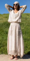 Woman outdoors in cream linen maxi dress with crochet sleeves and pockets, wearing sunglasses and headscarf