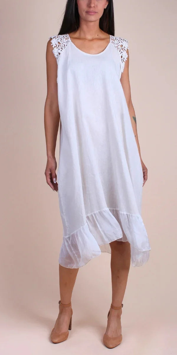 Woman wearing sleeveless white linen dress with crochet lace shoulders and ruffled hem