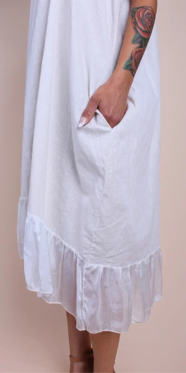 White linen dress with ruffled hem and pocket, arm with rose tattoo visible