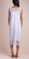 Back view of a woman wearing a white linen dress with lace shoulders and ruffle hem