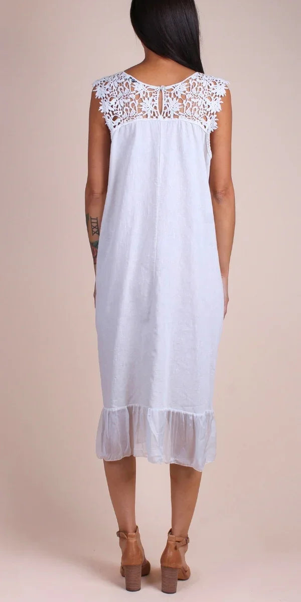 Back view of a woman wearing a white linen dress with lace shoulders and ruffle hem