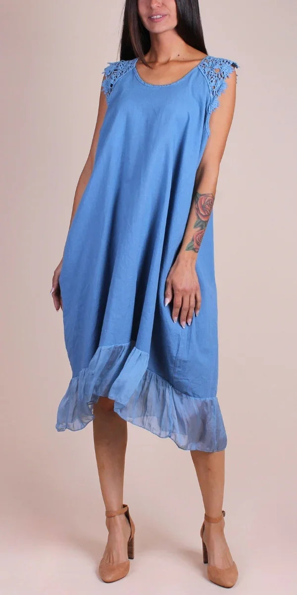 Woman wearing a blue sleeveless linen dress with lace shoulder detail and ruffled hem