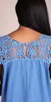 Back view of woman wearing blue linen top with crochet lace yoke and button closure