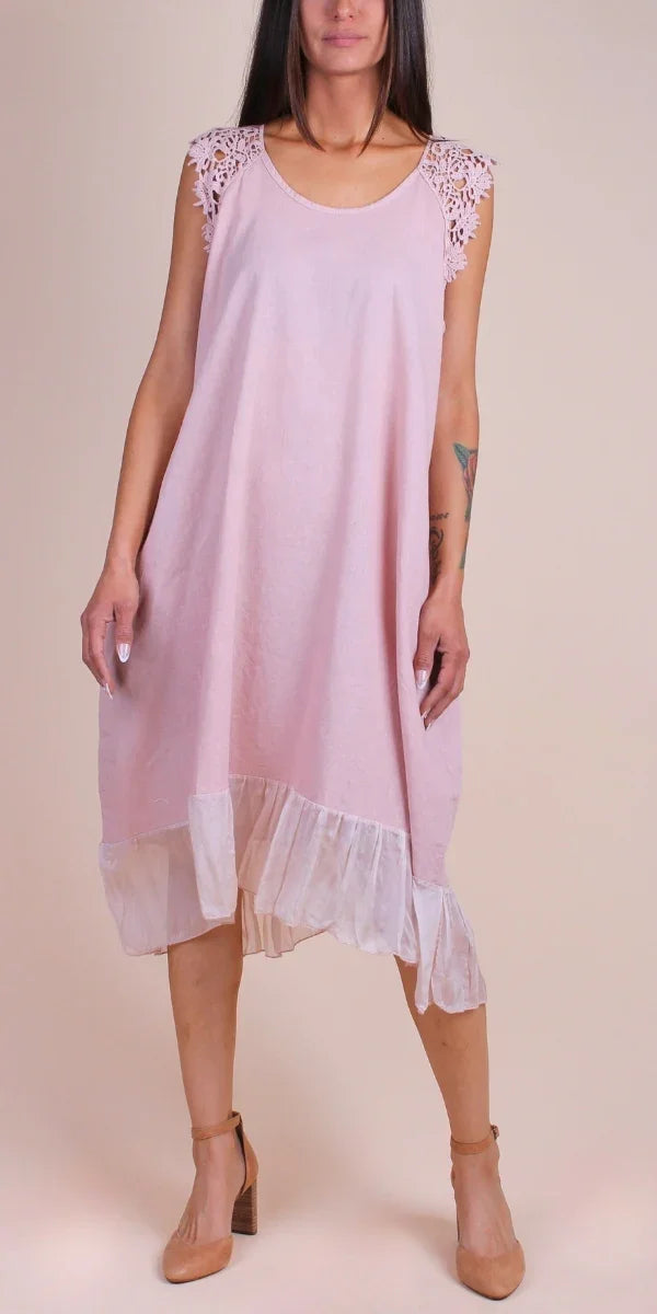 Woman in a light pink linen dress with lace sleeves and sheer ruffle hem, neutral background