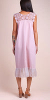 Woman wearing a light pink linen midi dress with lace yoke and ruffle hem, back view