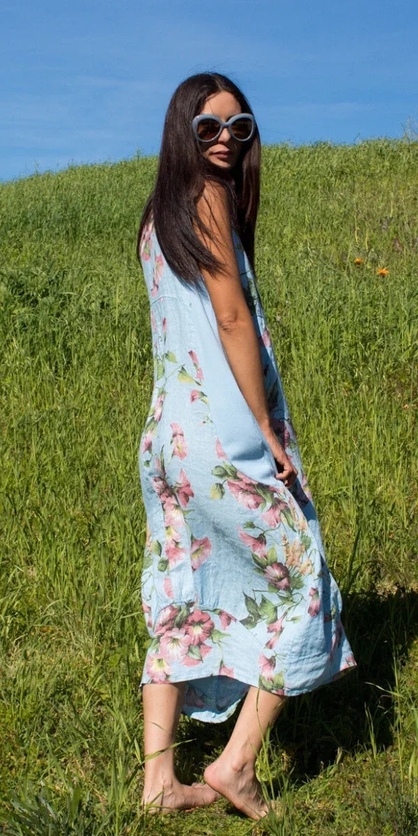 Woman in blue floral linen dress with sunglasses standing barefoot on grass outdoors