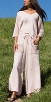 Woman wearing a light pink linen jumpsuit with crochet sleeves and pockets, standing outdoors