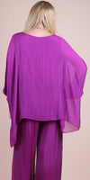 Woman wearing a flowy purple silk top and pants set, back view, studio background
