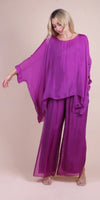 Woman wearing a loose magenta silk blouse and wide-leg pants, standing against beige background