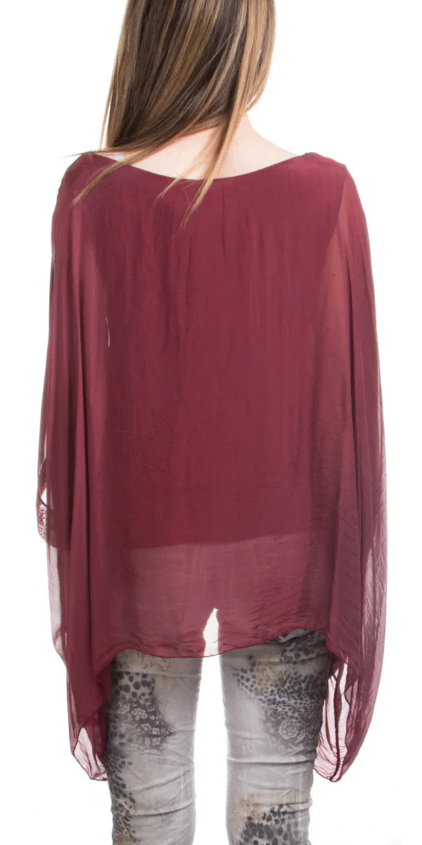 Back view of woman in sheer burgundy poncho blouse and patterned pants