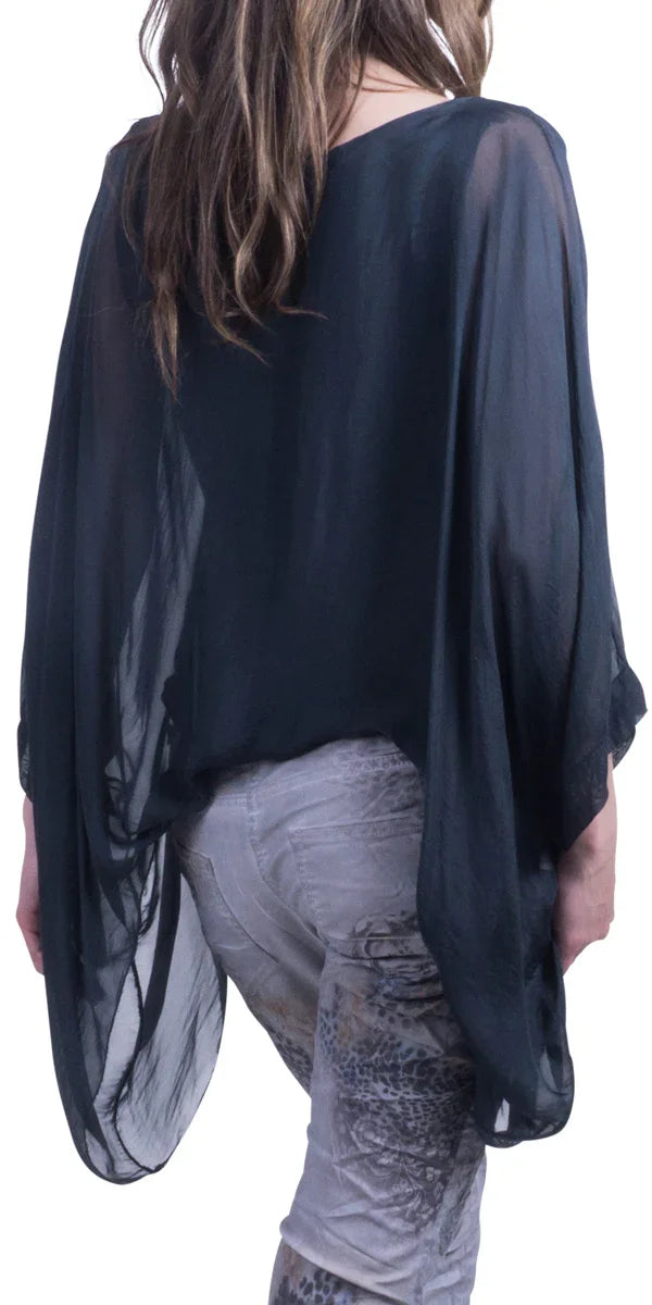 Woman wearing sheer black silk poncho top and patterned skinny pants, back view